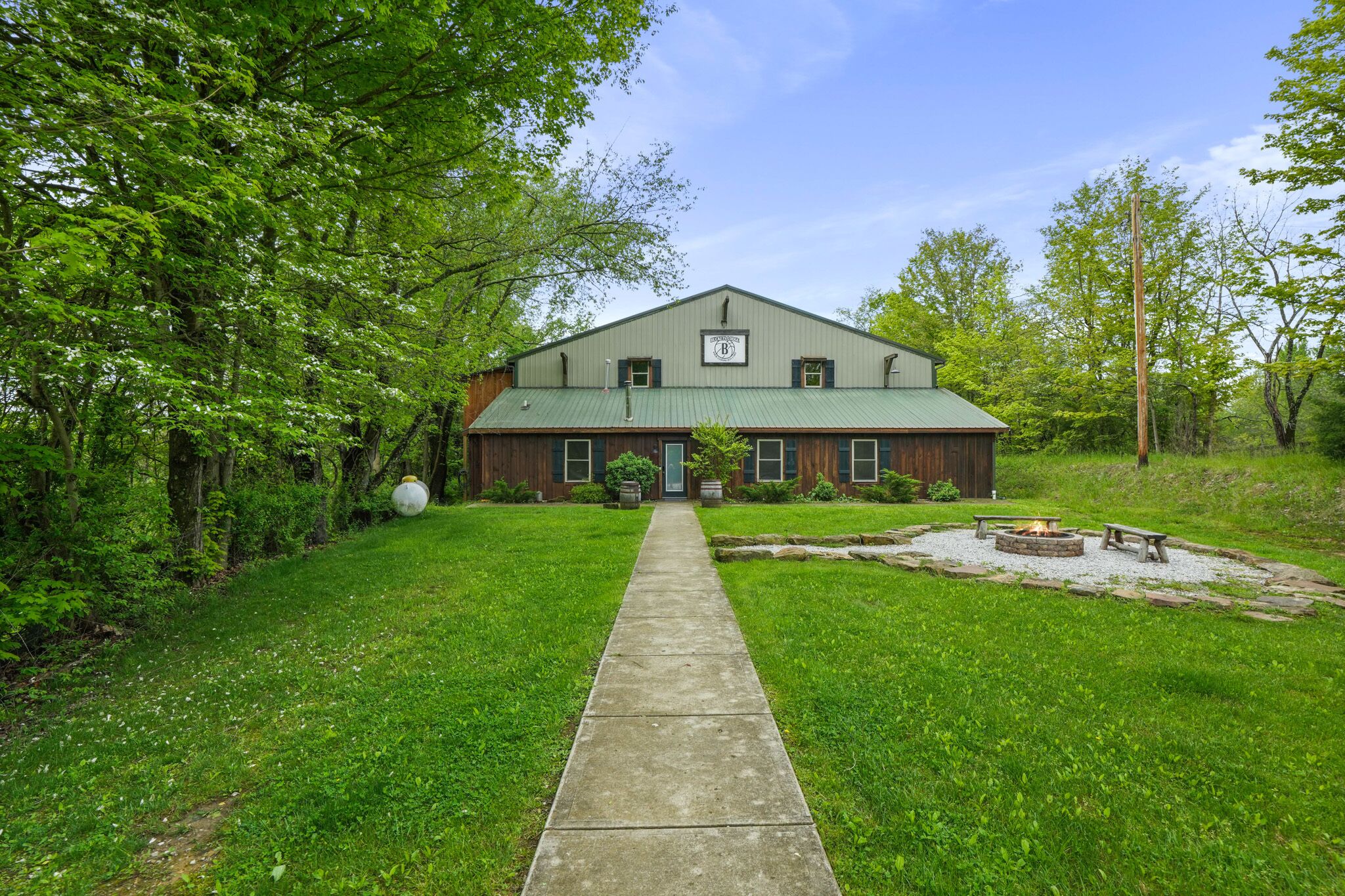 A two-story building with a green roof, a front door, and a pathway leading to a fire pit area.