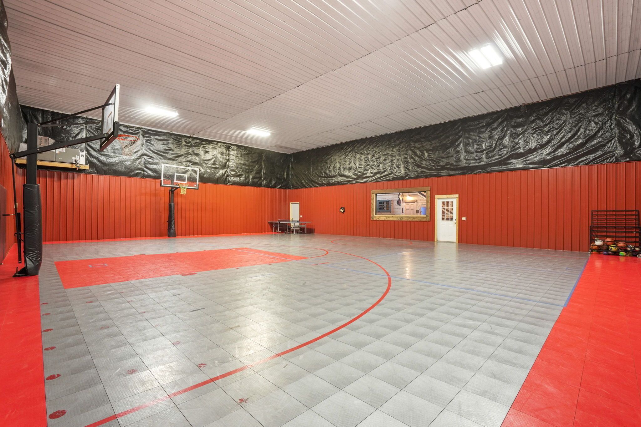 An indoor basketball court with a red and grey floor, a basketball hoop, and a bench.
