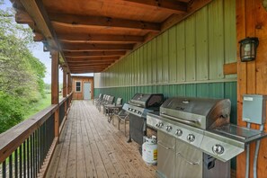 An outdoor deck with a covered area, multiple barbecue grills, and a view of the surrounding greenery. - Buckets Lodge | Sleeps 28, Theater & Basketball (Logan)