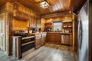 A rustic kitchen with wooden cabinets, a stainless steel refrigerator, and a dishwasher. - Buckets Lodge | Sleeps 28, Theater & Basketball (Logan)