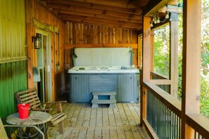 A wooden deck with a hot tub, a bench, and a table with a red bucket.