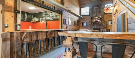 A rustic interior with a wooden bar area, stools, and a stone wall.