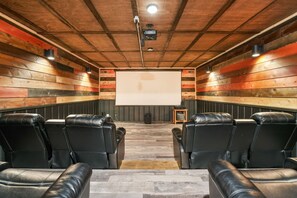 A home theater room with wooden panel walls, black leather recliner seating, a large screen, and a projector.