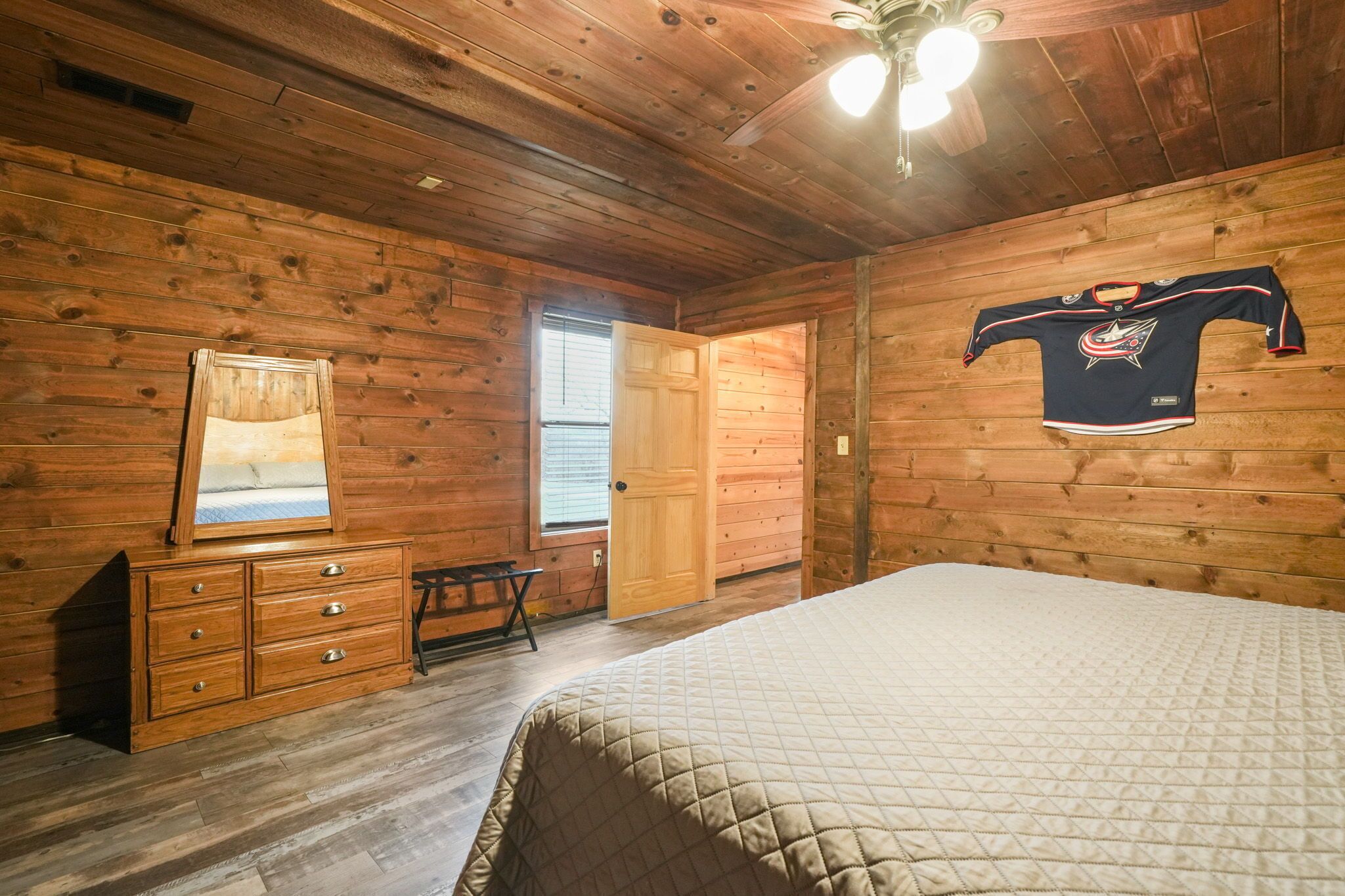 A wooden-paneled room with a bed, a dresser, a mirror, a door, and a hockey jersey on the wall.