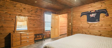 A wooden-paneled room with a bed, a dresser, a mirror, a door, and a hockey jersey on the wall.