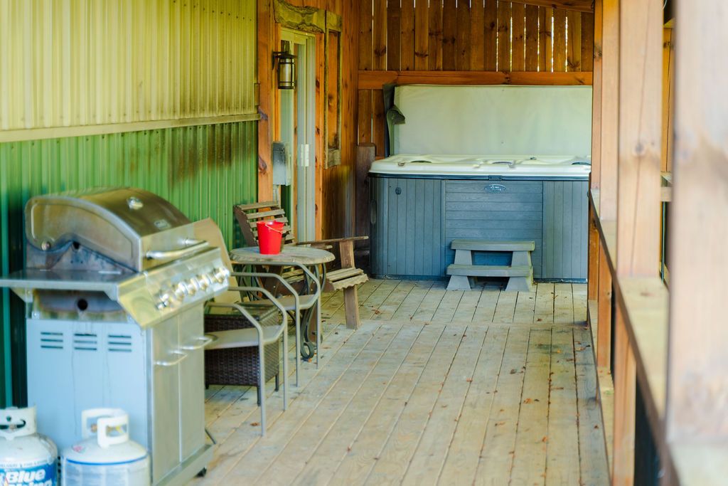 A wooden cabin interior with a barbecue grill, a hot tub, and a small table with chairs.