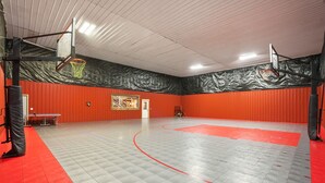 Una palestra al coperto con parquet rosso e grigio, due canestri da basket e una porta sullo sfondo.