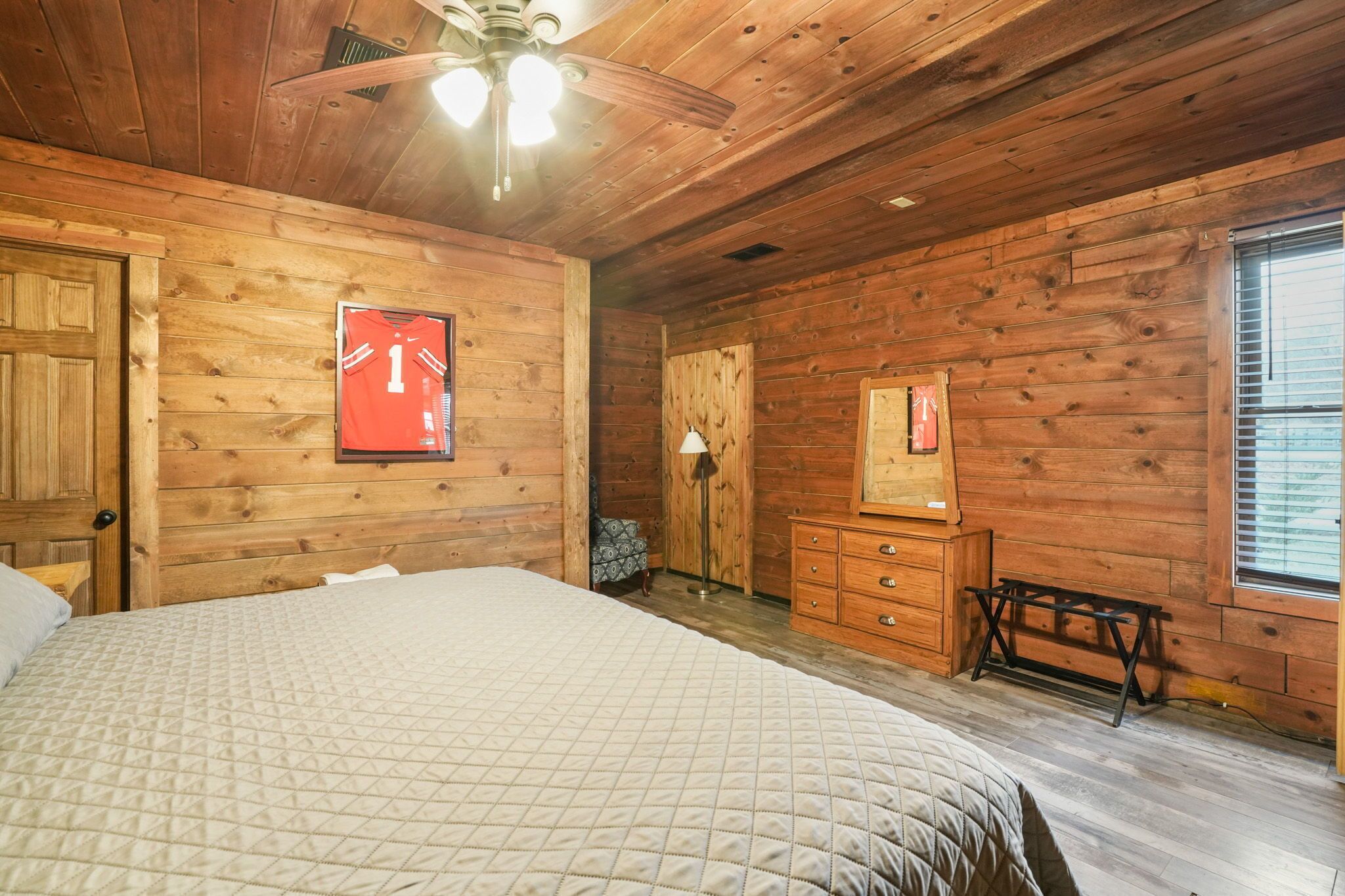 A wooden cabin bedroom with a bed, dresser, and a ceiling fan.