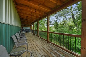 A covered outdoor deck with wooden flooring, metal chairs, and a grill. - Buckets Lodge | Sleeps 28, Theater & Basketball (Logan)