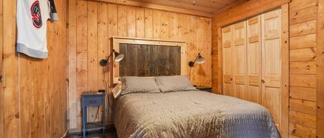A wooden-paneled bedroom with a bed, bedside lamps, a small table, and a hockey jersey on the wall.