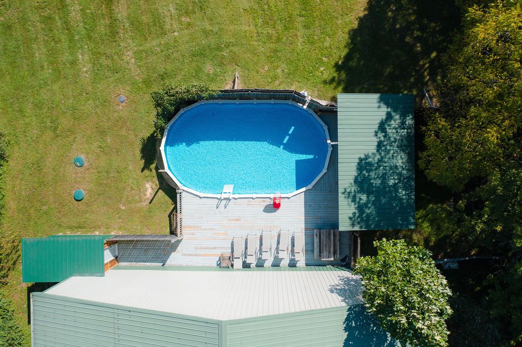 An aerial view of a swimming pool with a deck, surrounded by a grassy area and trees.