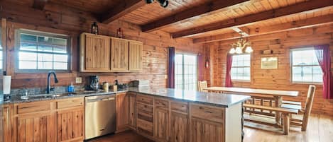 A wooden cabin interior with a kitchen, dining area, and a large window.