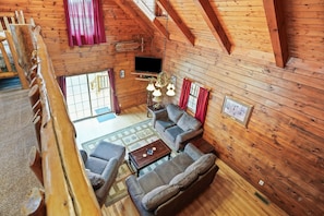 Interior acogedor de una cabaña de madera con cama en altillo, televisor, chimenea y comedor.
