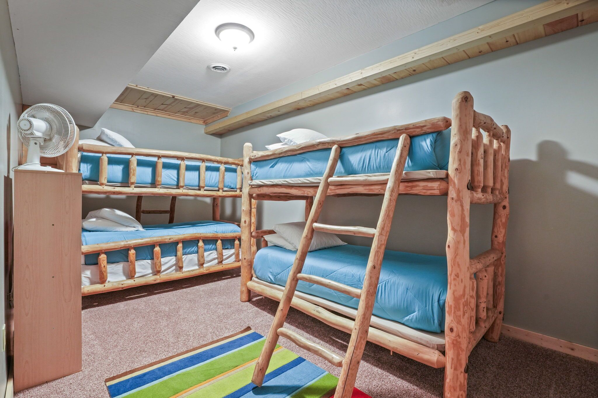Une chambre avec deux lits superposés, un ventilateur et un tapis rayé aux couleurs vives.