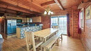 A rustic cabin interior with a wooden dining table, stone island, and a kitchen with a refrigerator and stove. - Pioneer Lodge | Hocking Hills, Sleeps 15, Hot Tub (Logan)