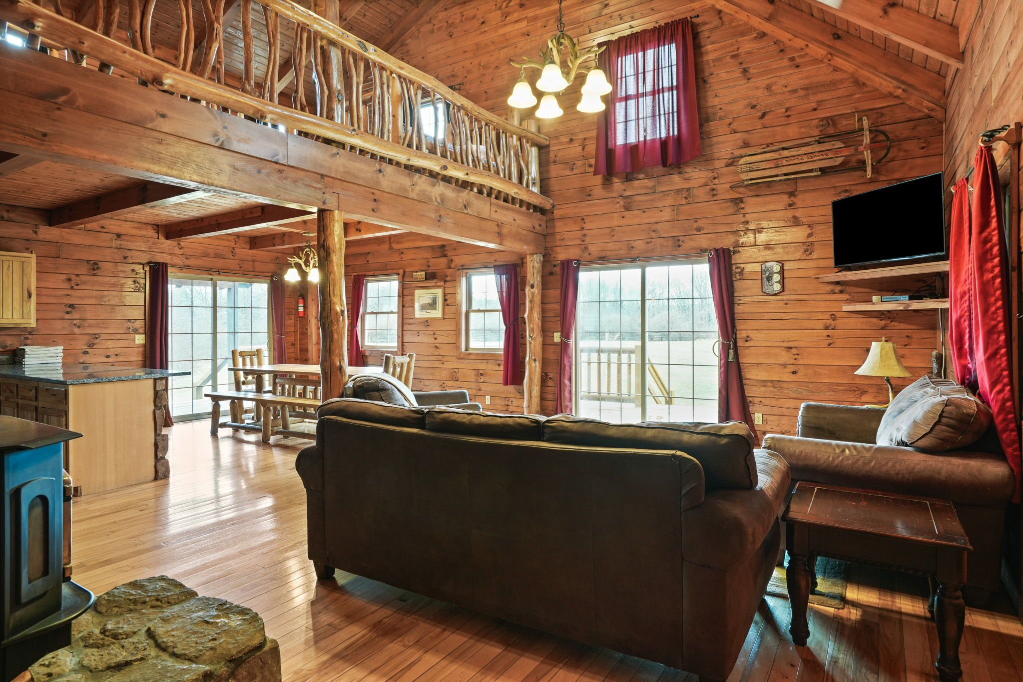 L’intérieur d’un chalet rustique, avec un plafond en bois, un coin repas, un canapé, un téléviseur et une cheminée en pierre.