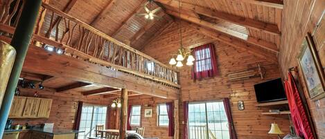 A spacious wooden cabin with a loft bedroom, a dining area, and a living room with a sofa and chairs.