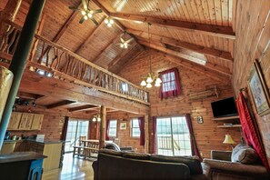 A spacious wooden cabin with a loft bedroom, a dining area, and a living room with a sofa and chairs. - Pioneer Lodge | Hocking Hills, Sleeps 15, Hot Tub (Logan)