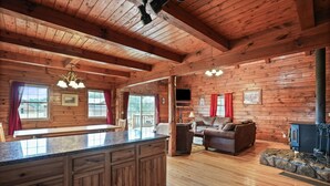 A wooden cabin interior with a kitchen, living area, and a stone fireplace. - Pioneer Lodge | Hocking Hills, Sleeps 15, Hot Tub (Logan)