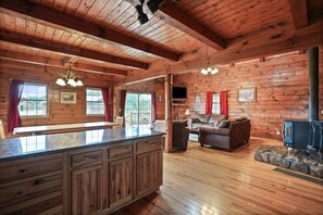 A wooden cabin interior with a kitchen, living area, and a stone fireplace.