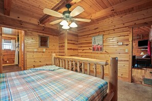 A wooden cabin room with a bed, a ceiling fan, a framed picture, and a television. - Pioneer Lodge | Hocking Hills, Sleeps 15, Hot Tub (Logan)