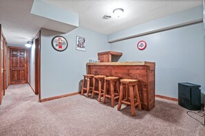 Una habitación de esquina con una barra de madera y taburetes, una puerta y un cubo de basura.