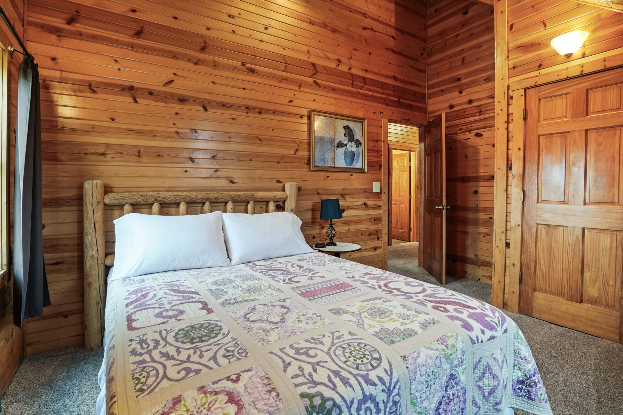 Un dormitorio de cabaña de madera con una cama, una mesita de noche, una lámpara y una puerta.