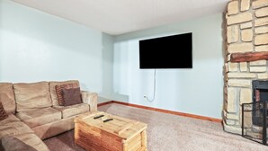 A living room with a stone fireplace, a beige sofa, and a flat-screen TV mounted on the wall. - Pioneer Lodge | Hocking Hills, Sleeps 15, Hot Tub (Logan)