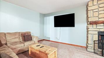 A living room with a stone fireplace, a beige sofa, and a flat-screen TV mounted on the wall.