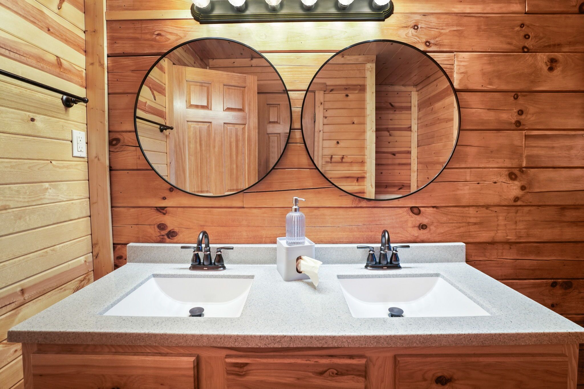 Baño de cabaña de madera con dos lavamanos, un espejo y dispensador de jabón.