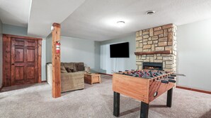 A cozy room with a foosball table, a stone fireplace, a flat-screen TV, and a wooden door. - Pioneer Lodge | Hocking Hills, Sleeps 15, Hot Tub (Logan)