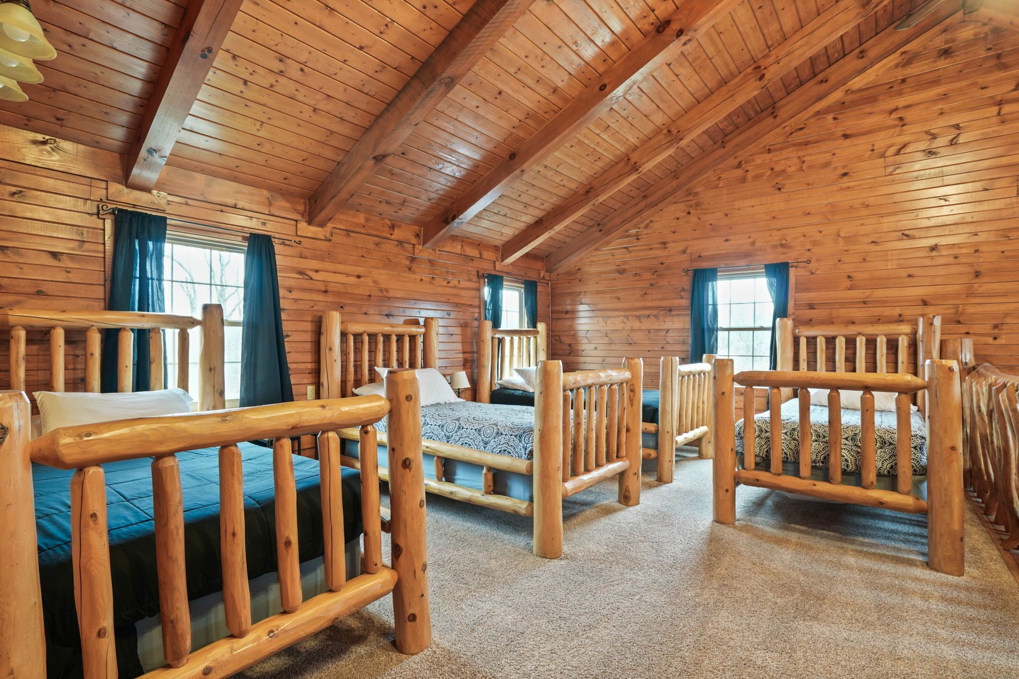 Ein Blockhausszimmer mit Holzbetten, einem Fenster und einer Decke mit Holzbalken.