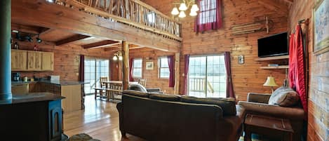 A spacious cabin with a loft bedroom, a cozy living area with a sofa and a fireplace, and a kitchen with wooden cabinets.