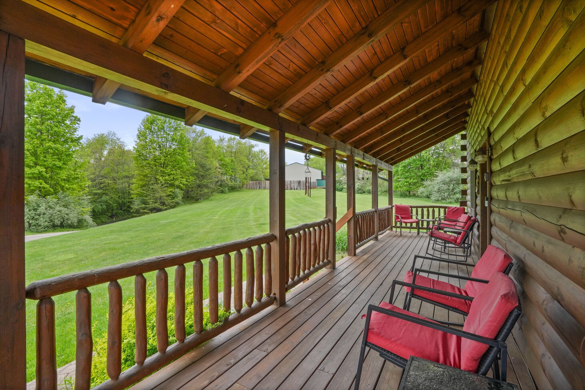 A wooden deck with red chairs and a view of a well-maintained lawn and trees.