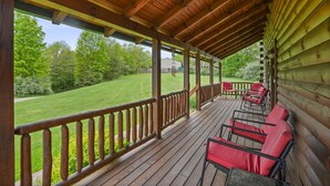 A wooden deck with red chairs and a view of a well-maintained lawn and trees. - Pioneer Lodge | Hocking Hills, Sleeps 15, Hot Tub (Logan)