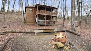 A wooden cabin with a balcony, a fire pit, and a deck. - Hide-A-Way Tiny House | Hocking Hills, Hot Tub (Logan)