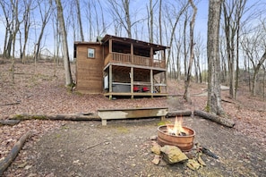 A wooden cabin with a balcony, a fire pit, and a deck.