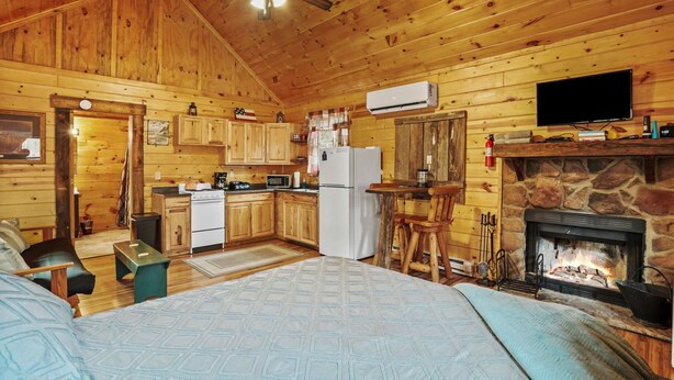 A log cabin interior with a kitchen, dining area, and a fireplace. - Hide-A-Way Tiny House | Hocking Hills, Hot Tub (Logan)