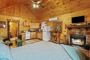A log cabin interior with a kitchen, dining area, and a fireplace. - Hide-A-Way Tiny House | Hocking Hills, Hot Tub (Logan)