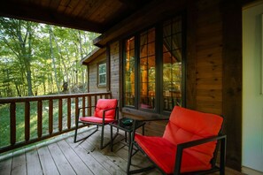 A wooden cabin with a porch, two red chairs, and a table.