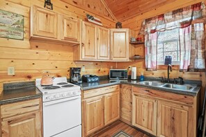 A cabin-style kitchen with wooden cabinets, a stove, a microwave, and a sink. - Hide-A-Way Tiny House | Hocking Hills, Hot Tub (Logan)