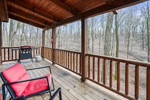 Une terrasse en bois avec une chaise rouge et un barbecue, donnant sur une zone boisée.