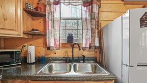 A kitchen with wooden cabinets, a double sink, a microwave, and a refrigerator. - Hide-A-Way Tiny House | Hocking Hills, Hot Tub (Logan)