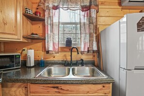 A kitchen with wooden cabinets, a double sink, a microwave, and a refrigerator.