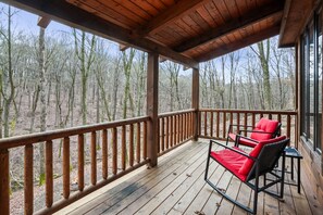 Eine Holzterrasse mit Geländer, zwei rote Sitzgelegenheiten und Blick auf einen Wald.