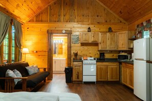 A cabin interior with a wooden interior, a sofa, a kitchen area with a stove, and a refrigerator.
