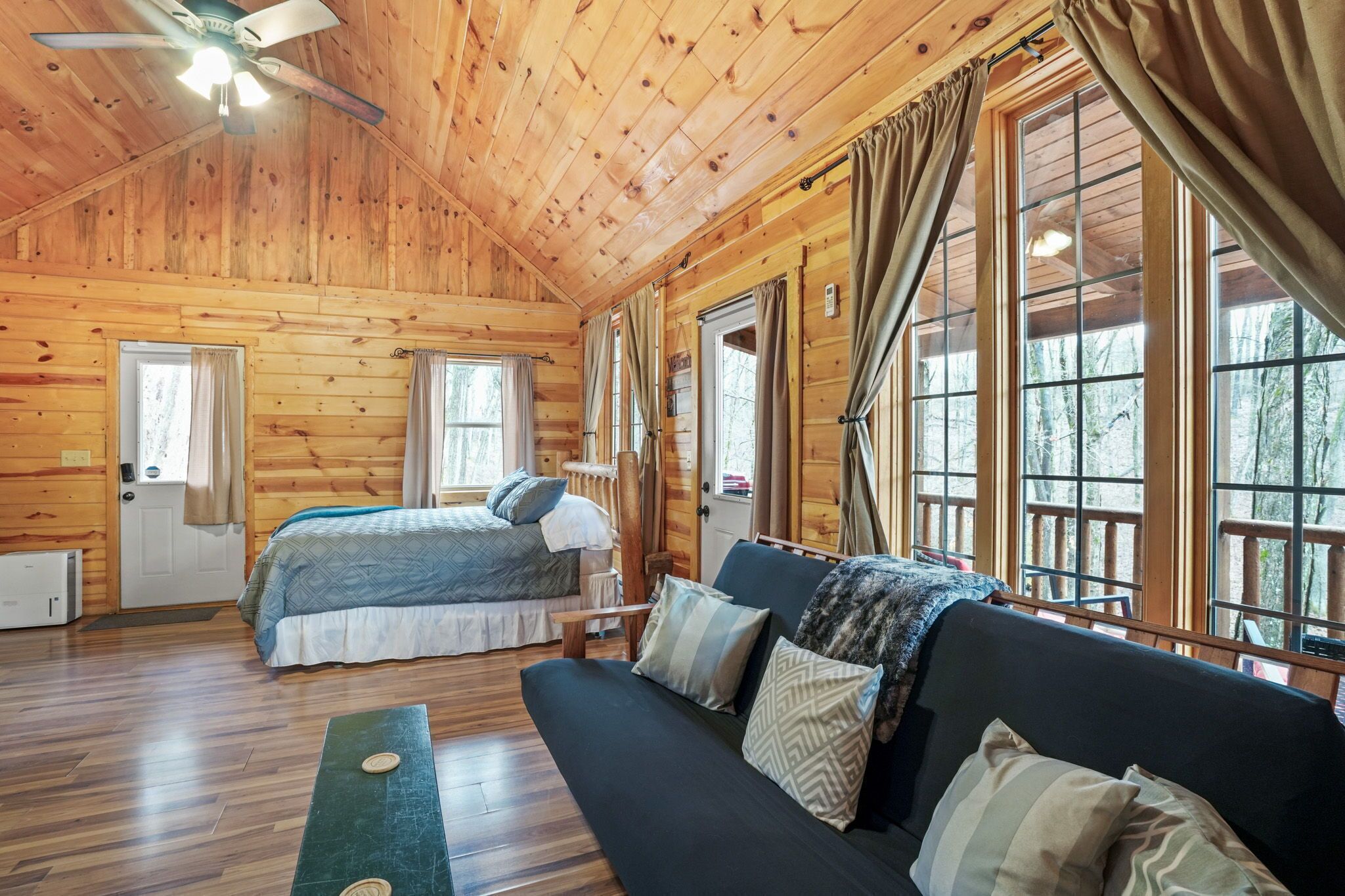 Une cabane en bois avec un lit, un canapé et de grandes fenêtres.