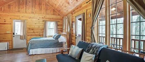 Une cabane en bois avec un lit, un canapé et de grandes fenêtres.