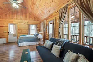A wooden cabin with a bed, a sofa, and large windows.
