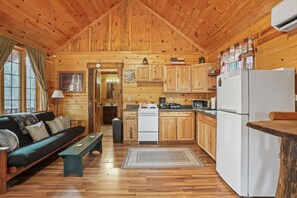 A cabin-style kitchen with wooden walls and floors, a stove, refrigerator, and a dining area with a bench.